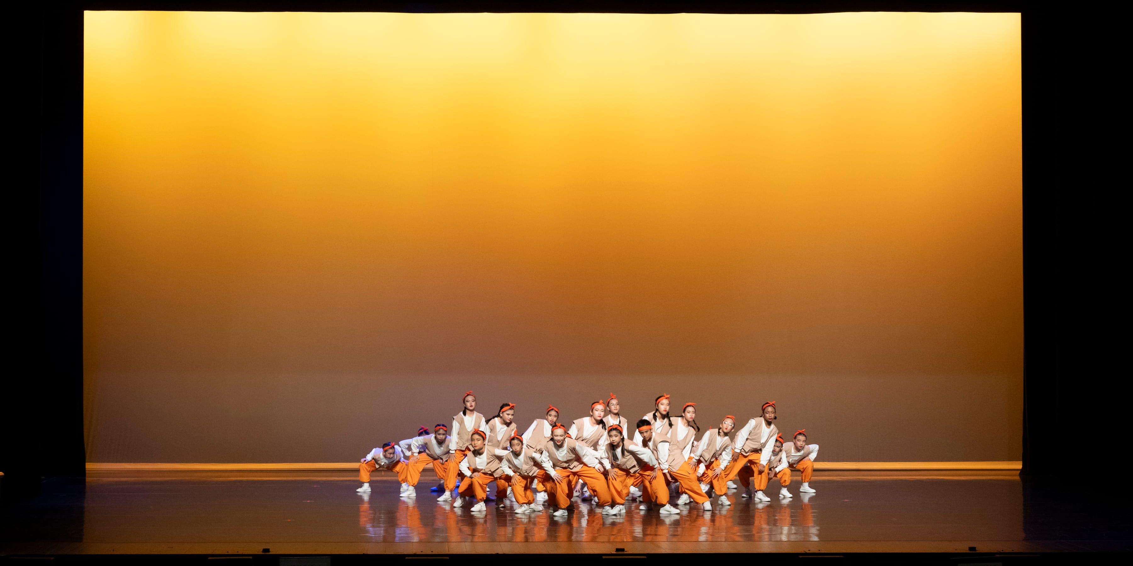 A group of students in orange tracksuits performing a dance on stage